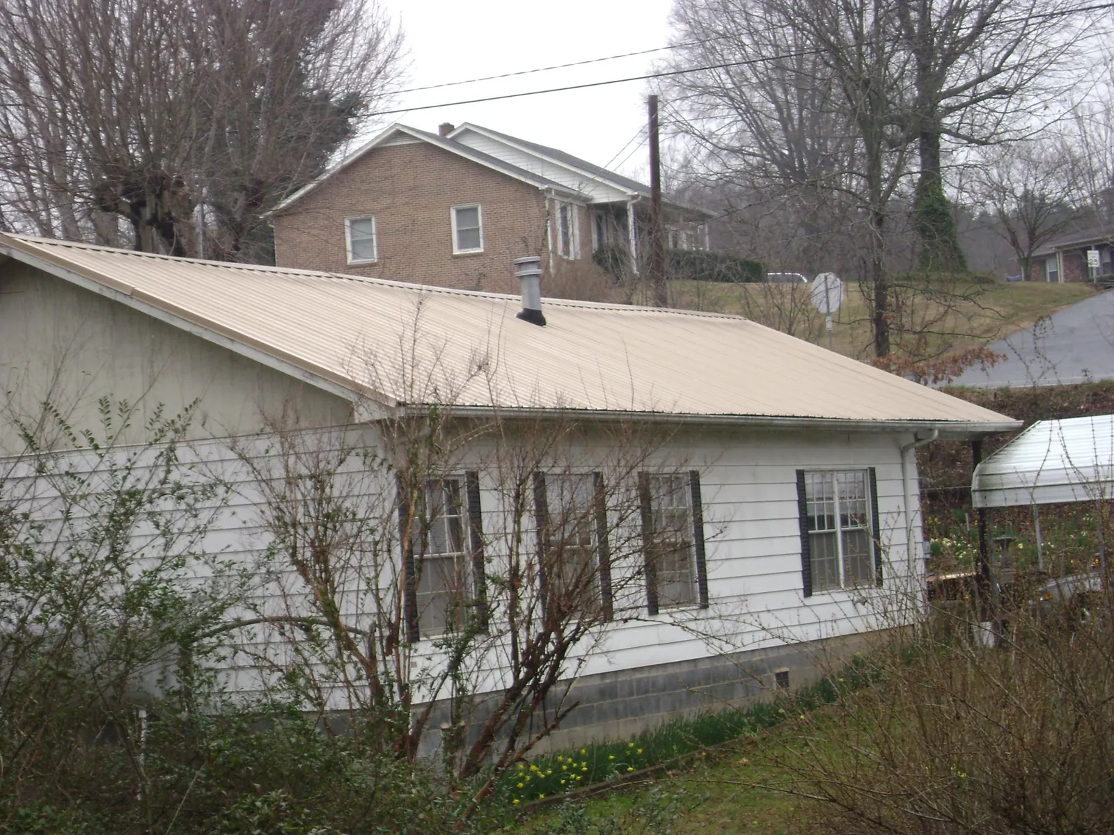 Tan metal roof on a white sided house set into a hillside — Commercial Roofing by Roofing Brothers in Madisonville