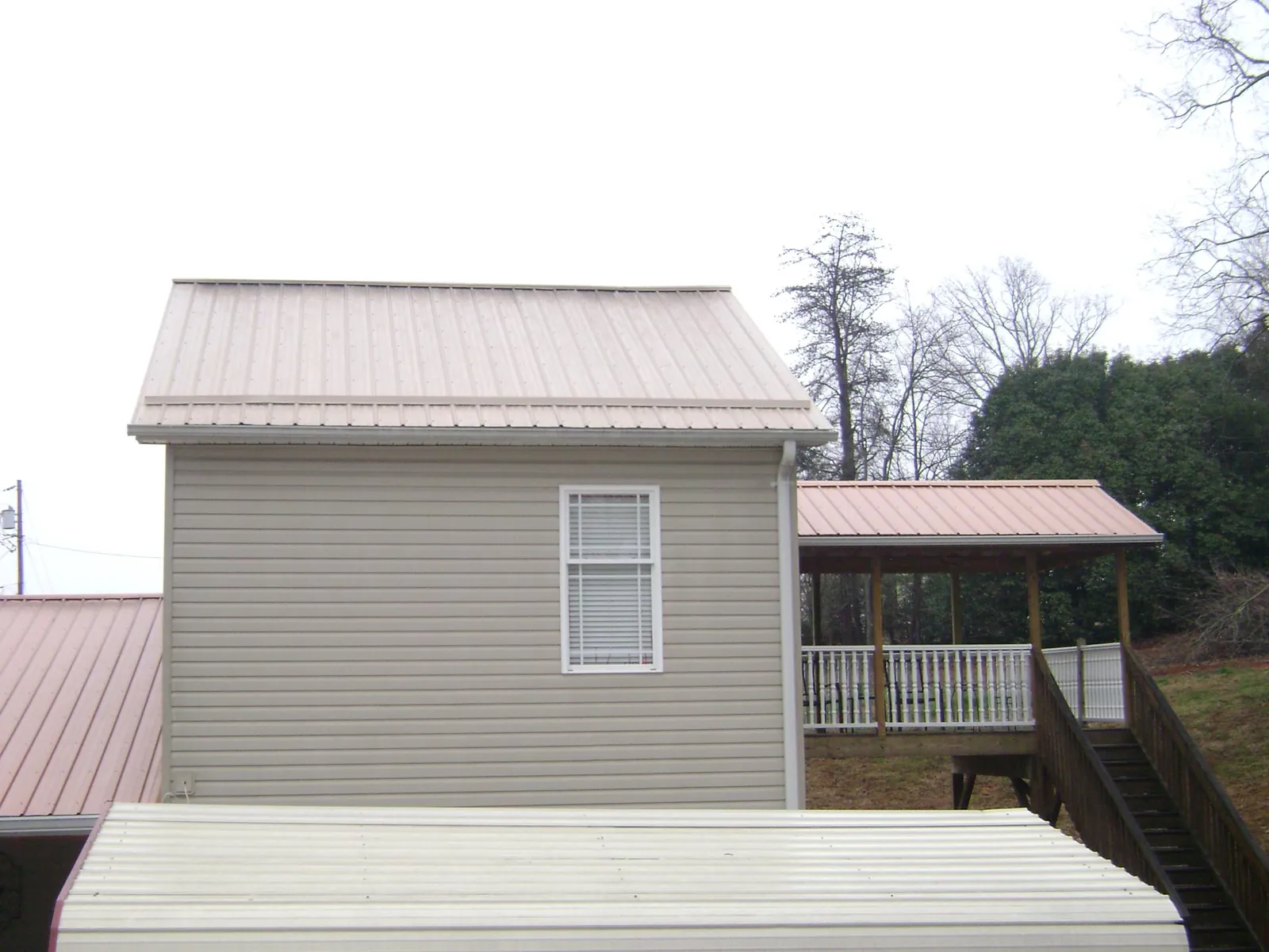 Tan metal roofs on a two story addition and attached porch, from a Roof Replacement job in Madisonville